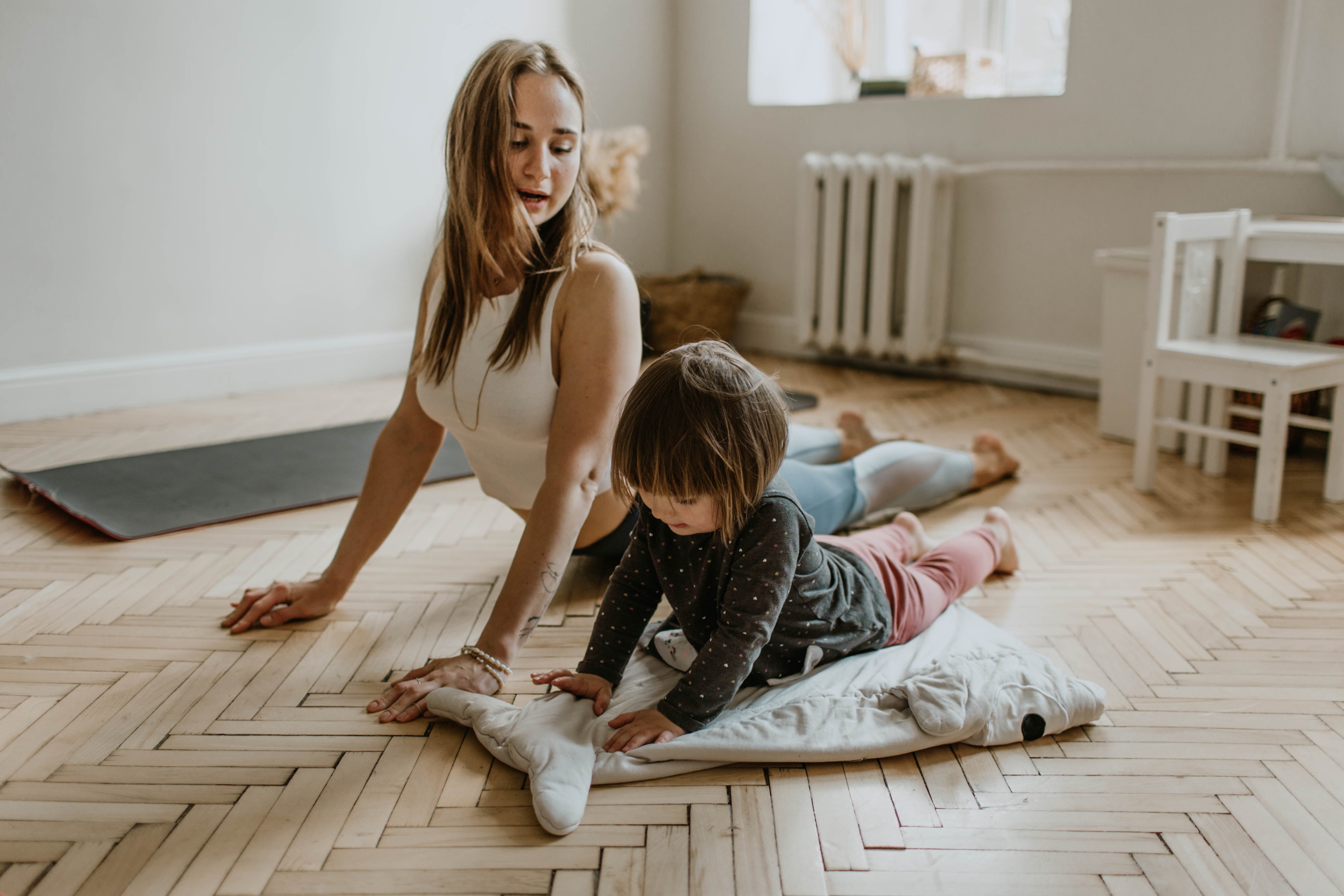 A mother and child playing on a wooden tile floor.